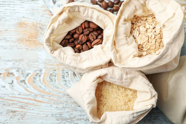 Cotton eco bags with cereals and coffee beans on wooden table, flat lay