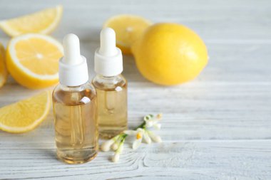 Beyaz ahşap masa üzerinde turunçgil yağı, çiçek ve limon şişeleri. Metin için boşluk
