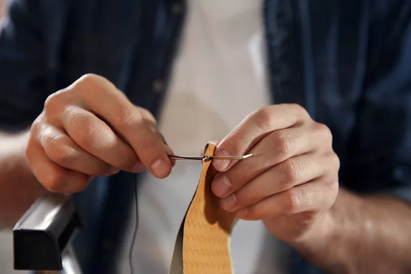 Man sewing piece of leather in workshop, closeup