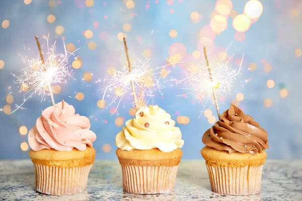 Hermosos cupcakes de cumpleaños con bengalas en la mesa contra el desenfoque —  Fotos de Stock