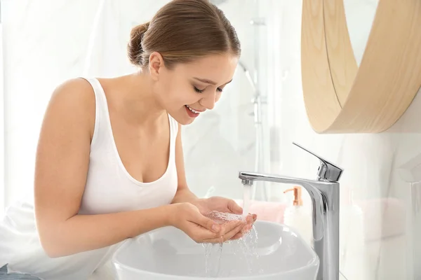 Young woman washing face with tap water in bathroom — Stock Photo, Image