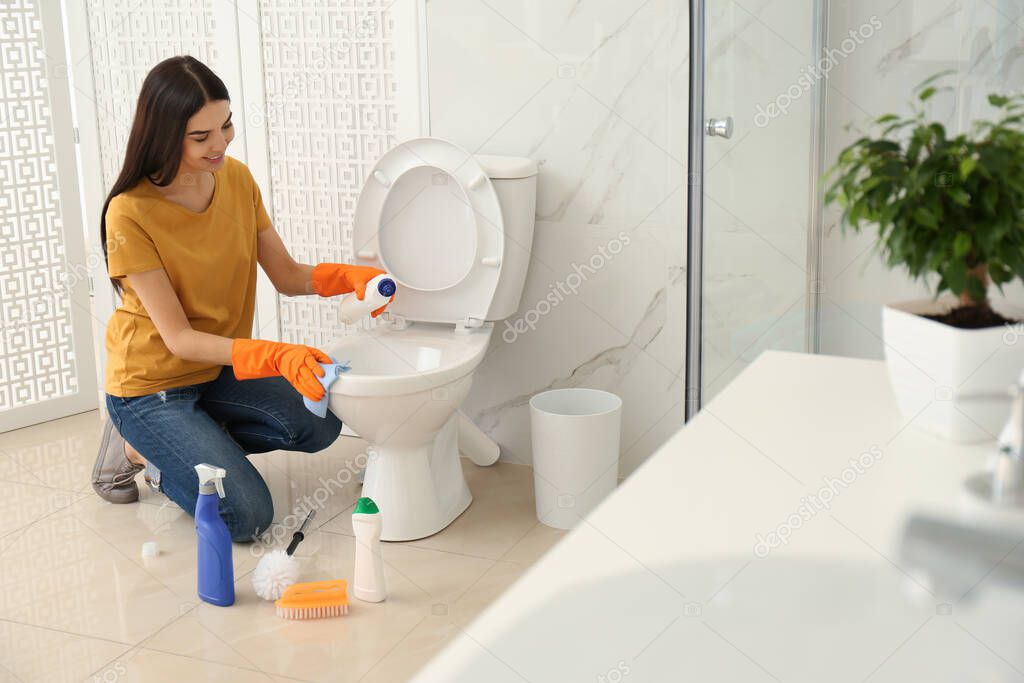 Young woman cleaning toilet bowl in bathroom