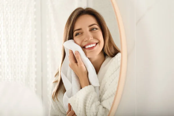 Mladá žena otírání tvář s ručníkem v blízkosti zrcadla v koupelně — Stock fotografie