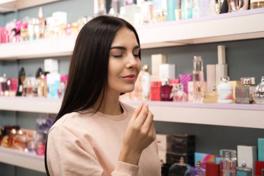 Güzel genç bir kadın dükkanda parfüm seçiyor.