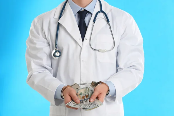Doctor in handcuffs with bribe on light blue background, closeup — Stock Photo, Image