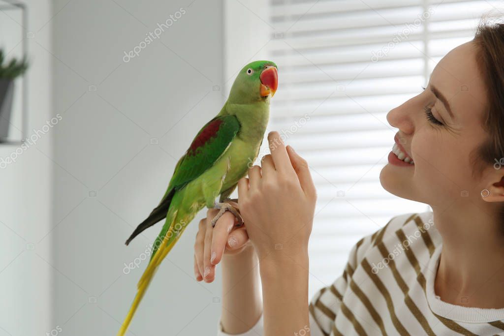 Young woman with cute Alexandrine parakeet indoors