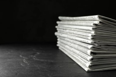 Stack of newspapers on dark stone table, space for text. Journal