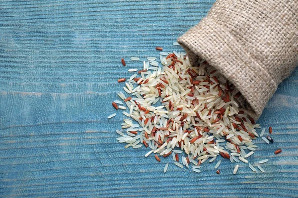 Mix of brown and polished rice in bag on blue wooden table, top view