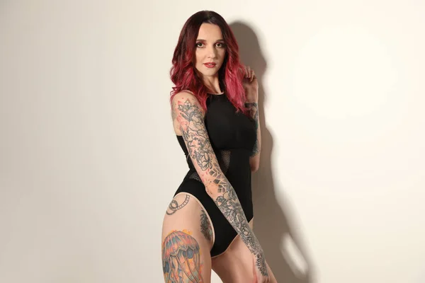 Beautiful woman with tattoos on body against light background