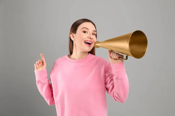 Jovem mulher com megafone em fundo cinza — Fotografia de Stock