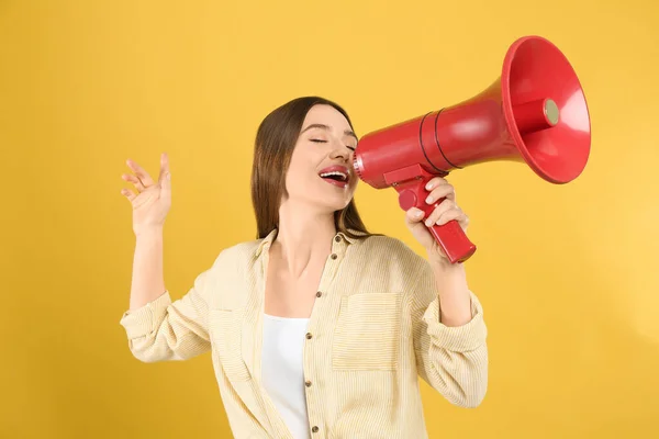 Young woman with megaphone on yellow background — Stock Photo, Image