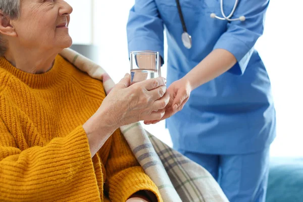 Care worker giving water to elderly woman in geriatric hospice, — 스톡 사진