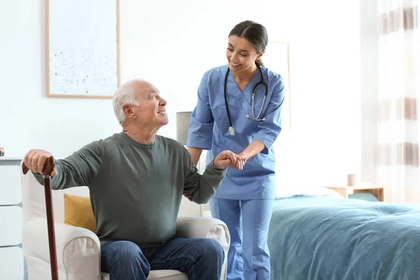 Care worker helping elderly man with stick in geriatric hospice — 스톡 사진