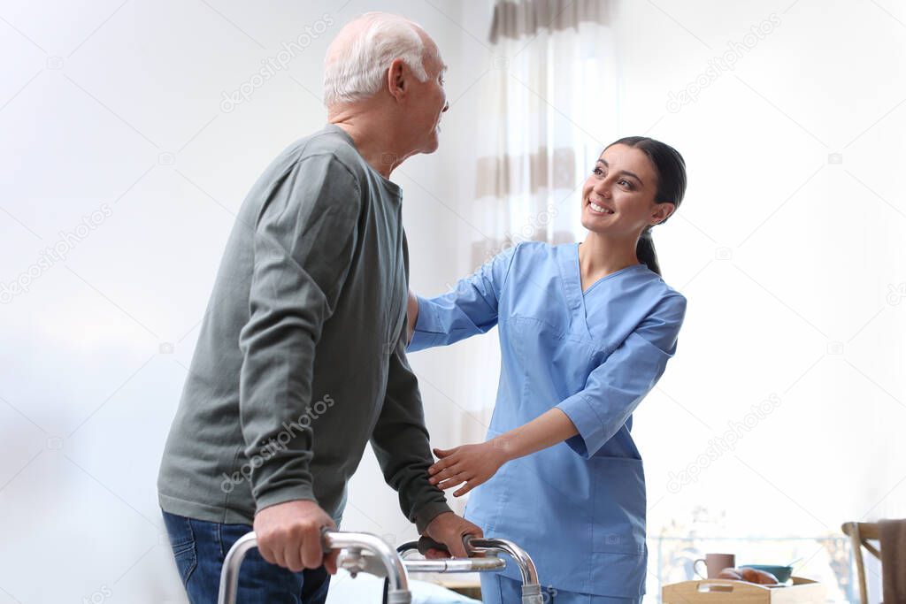 Care worker helping elderly man with walker in geriatric hospice