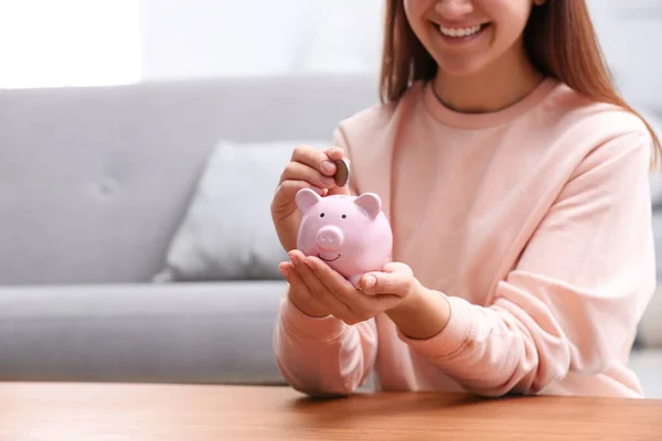 Mujer poniendo moneda en alcancía en la mesa de madera, primer plano — Foto de Stock