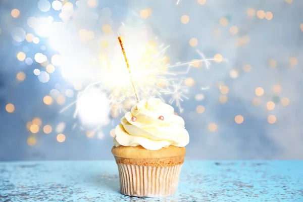 Bonito cupcake de aniversário com sparkler na mesa azul contra b — Fotografia de Stock