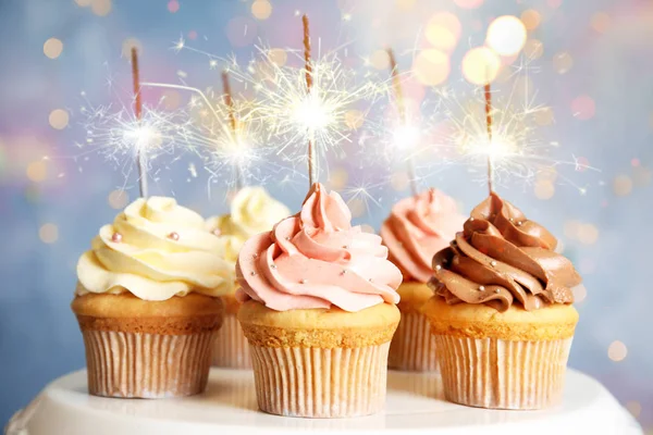 Hermosos cupcakes de cumpleaños con bengalas en el stand contra el desenfoque —  Fotos de Stock