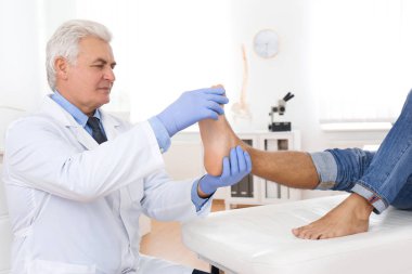 Erkek ortopedist klinikte hastanın ayağını kontrol ediyor.