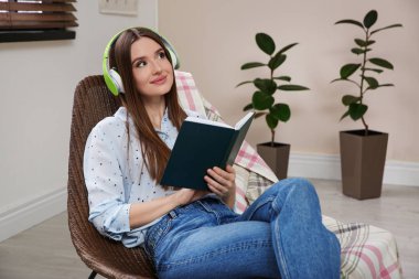 Evdeki sandalyede sesli kitap dinleyen bir kadın.