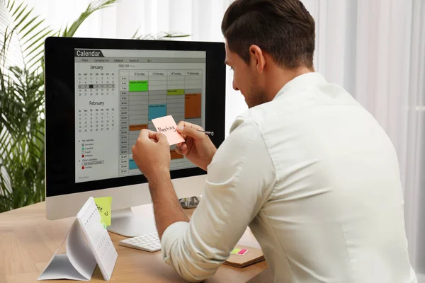 Hombre guapo utilizando la aplicación de calendario en el ordenador en la oficina —  Fotos de Stock