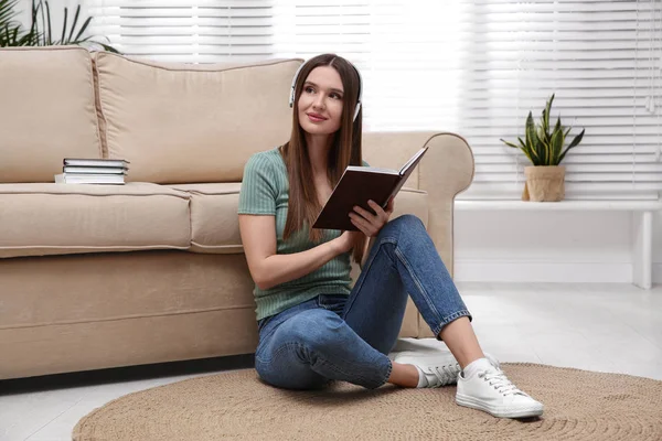 Mujer escuchando audiolibro cerca de sofá en casa —  Fotos de Stock