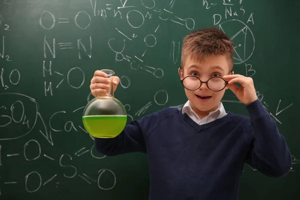 Schoolboy segurando frasco perto de quadro-negro com fórmulas químicas — Fotografia de Stock