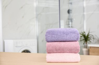 Stack of fresh towels on wooden table in bathroom. Space for tex