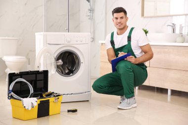 Repairman with clipboard and toolbox near washing machine in bat