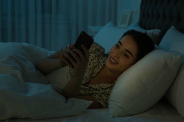 Gece yatakta akıllı telefona bağımlı genç bir kadın.