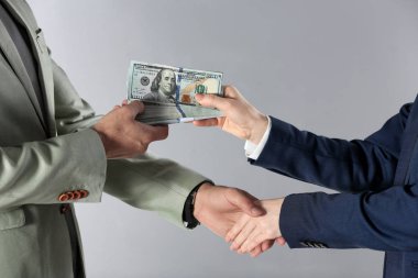 Bir kadın bir erkekle tokalaşıyor ve gri arka planda rüşvet teklif ediyor.