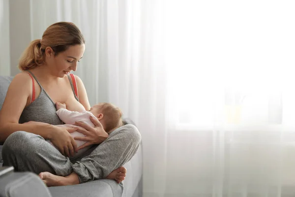 Jovem mulher amamentando seu bebê em casa. Espaço para texto — Fotografia de Stock