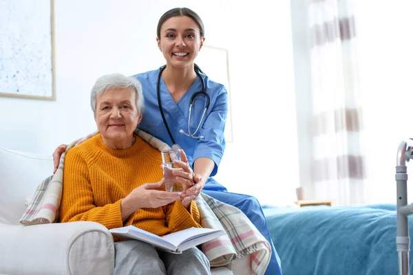 Zorgverlener geeft water aan oudere vrouw in geriatrisch hospice — Stockfoto