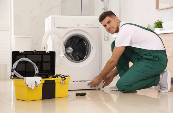 Professional plumber repairing washing machine in bathroom