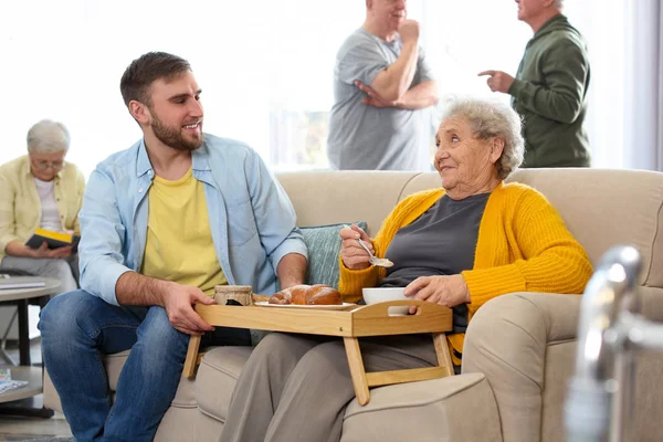 Jongeman serveert diner voor oudere vrouw in geriatrische hospice. — Stockfoto