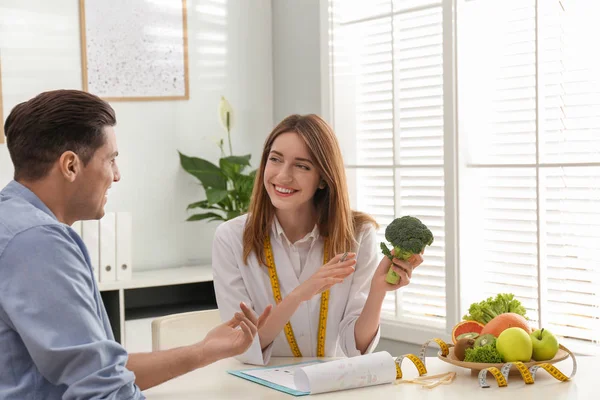 Young nutritionist consulting patient at table in clinic — Stock Photo, Image