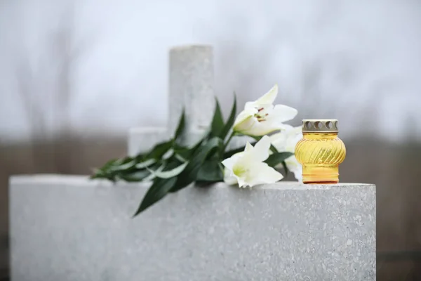 Bílé lilie a svíčka na světle šedé žulové náhrobní kámen venku — Stock fotografie