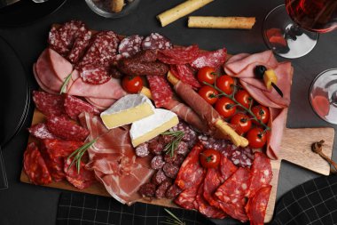 Tasty ham with other delicacies served on black table, flat lay