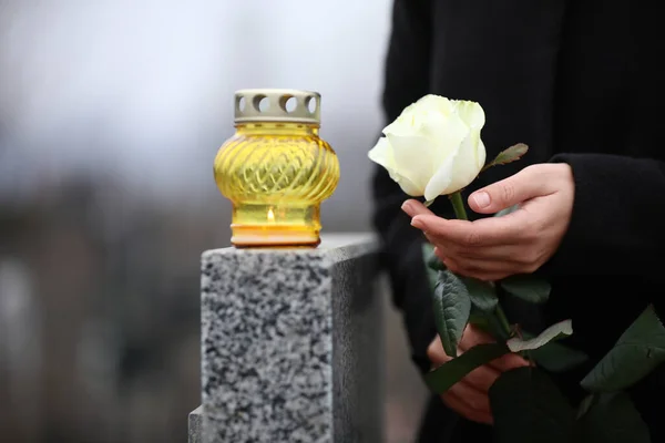 Kobieta trzyma białą różę w pobliżu szarego granitu nagrobek ze świecą — Zdjęcie stockowe