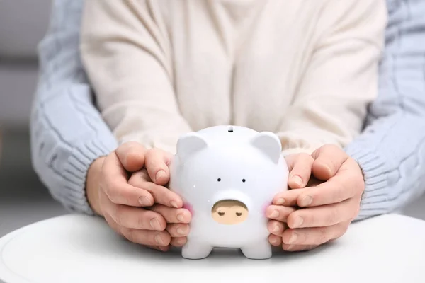 Couple with piggy bank at white table, closeup