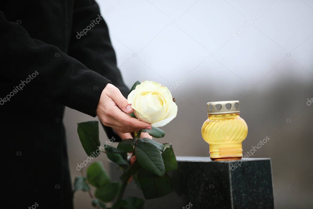 Woman holding white rose near black granite tombstone with candl