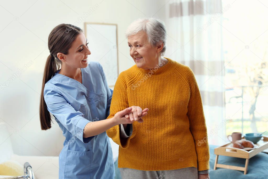 Care worker helping elderly woman to walk in geriatric hospice