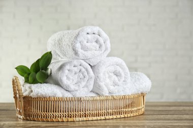 Yuvarlak banyo havluları ve ahşap masanın üzerinde yeşil bir dal olan sepet.