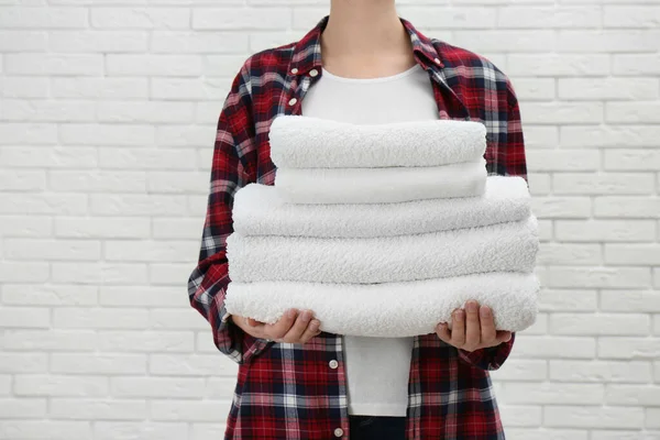 Mujer sosteniendo toallas frescas contra la pared de ladrillo blanco, primer plano — Foto de Stock