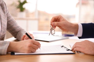 Real estate agent giving key with trinket to client in office, c