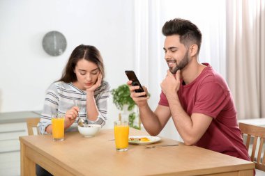 Young man preferring smartphone over his girlfriend at home clipart
