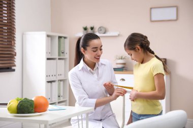 Professional nutritionist measuring waist of little girl in offi