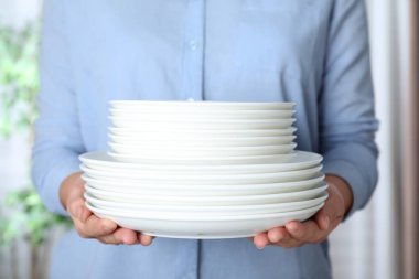 Kadın arka planda temiz tabak yığını tutuyor, kapat