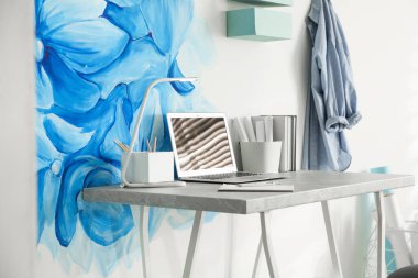 Stylish workplace with blue flowers painted on wall. Floral patt