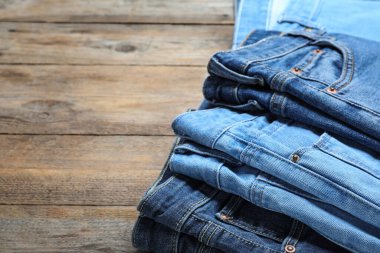 Collection of stylish jeans on wooden background, closeup. Space
