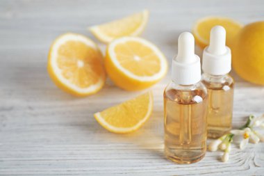 Beyaz ahşap masa üzerinde turunçgil yağı, çiçek ve limon şişeleri. Metin için boşluk